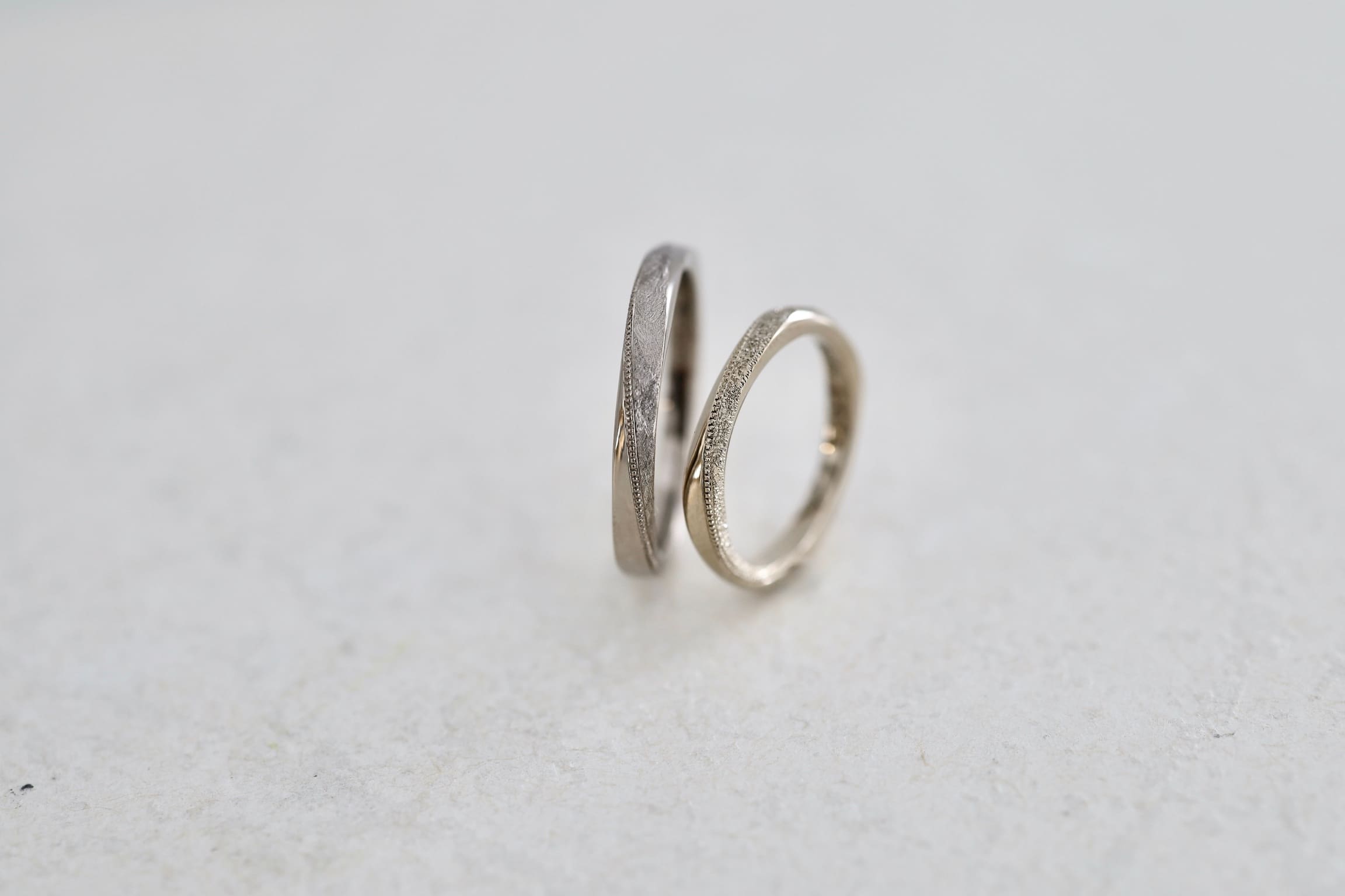 ひねり（ねじり）に沿ってミルグレインを施した結婚指輪。輝きのある加工と落ち着いた質感の組み合わせ。ホワイトゴールドとシャンパンゴールド