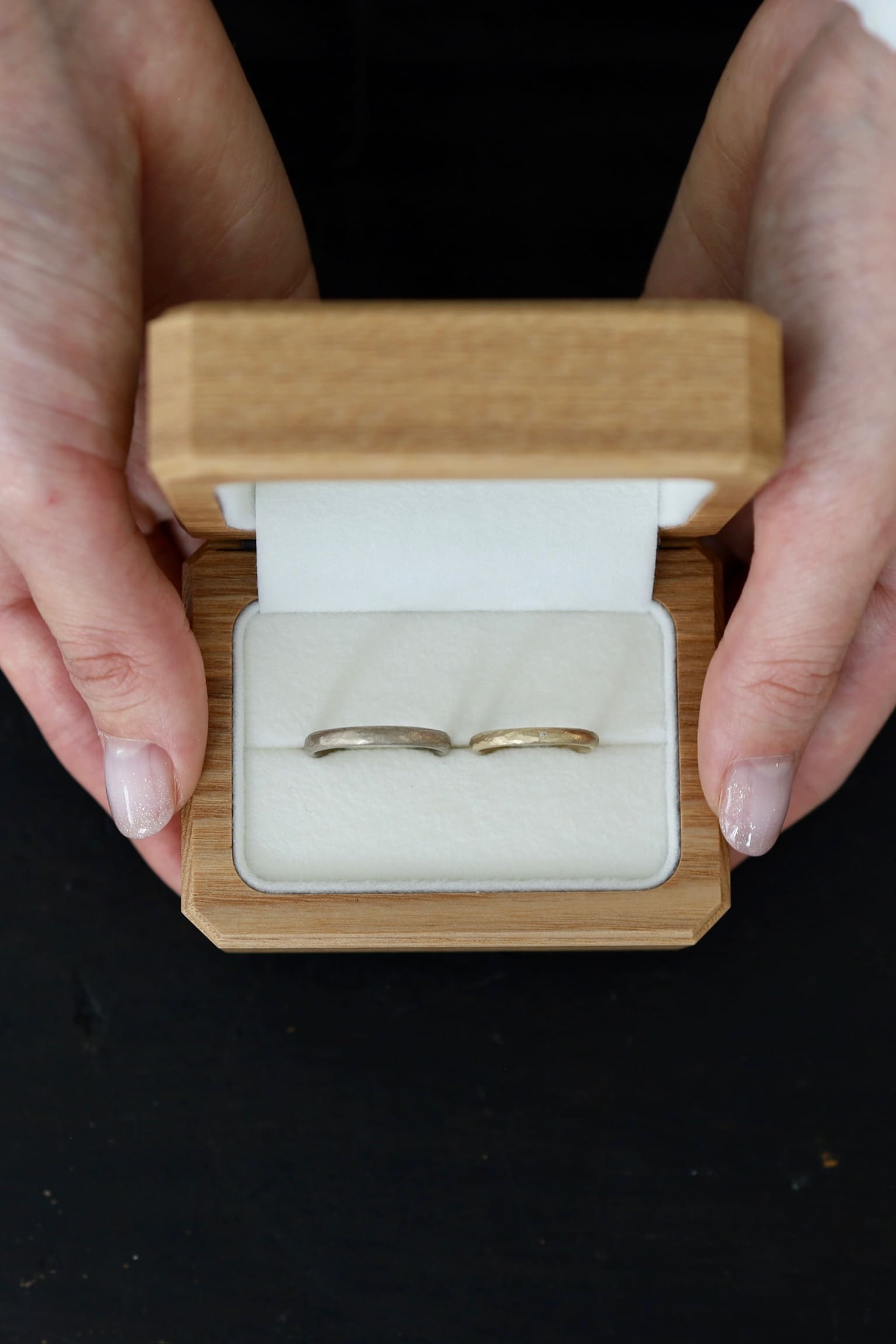 木製リングケースに収めたアンティークな結婚指輪２本を、両手で包むように持った写真